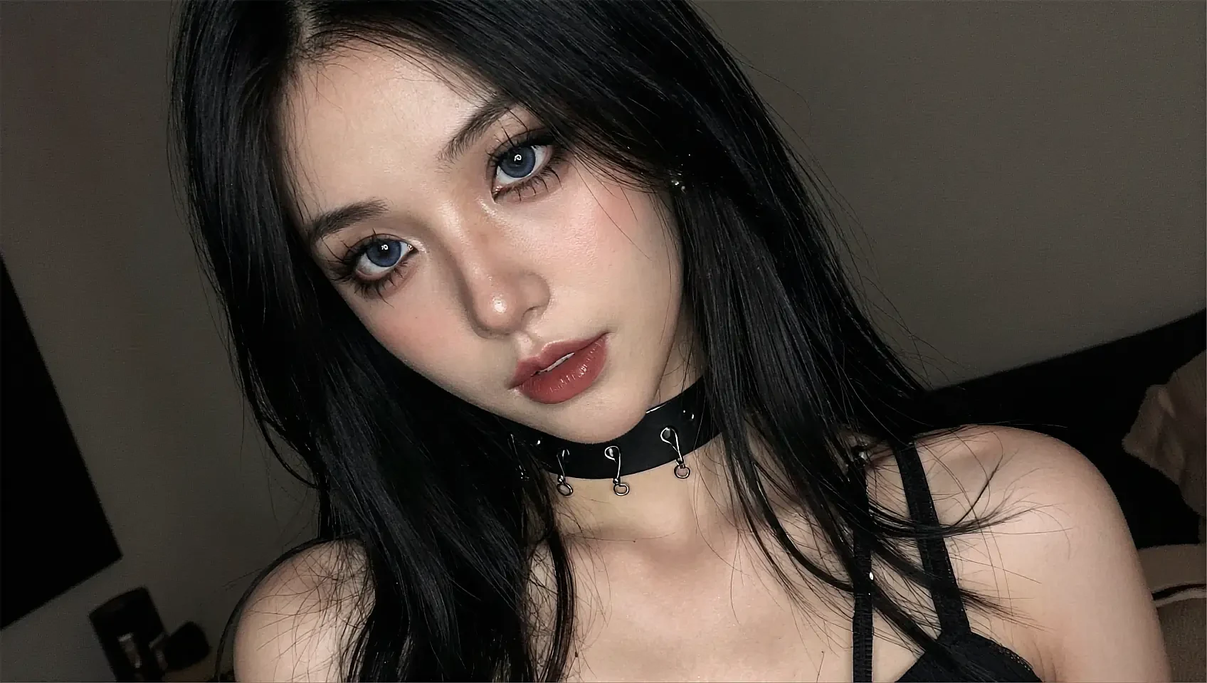 Close-up portrait of a dark-haired woman wearing a studded choker in a dim bedroom
